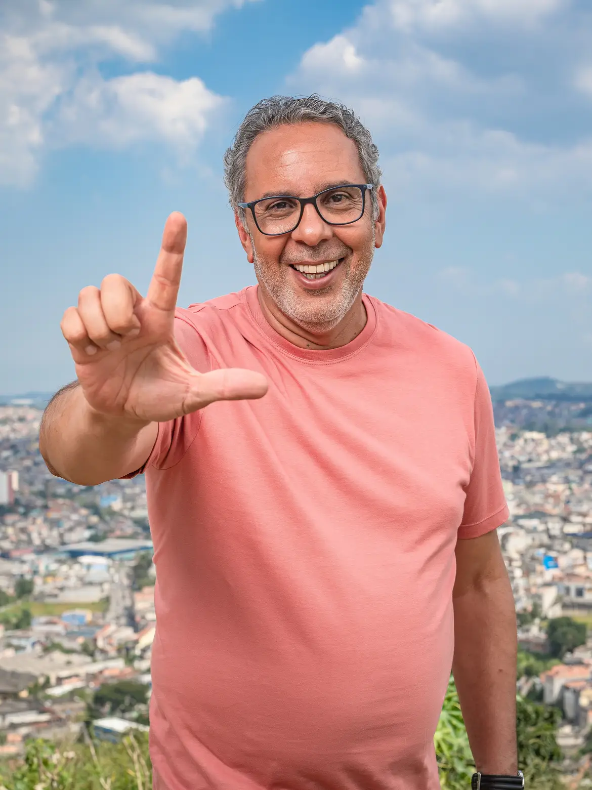 Rômulo Fernandes sorrindo com a mão erguida, com a cidade ao fundo.